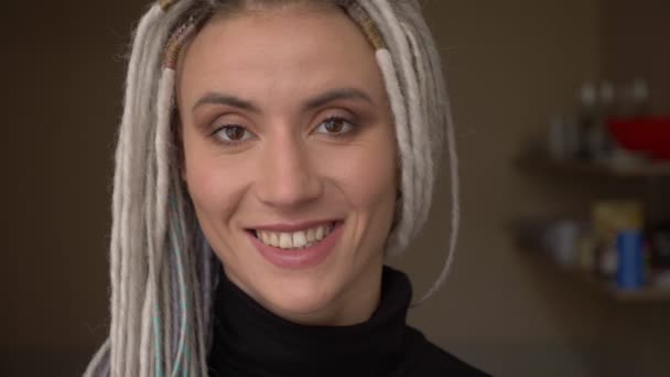 Съемки крупным планом молодой привлекательной кавказской хипстерки с белокурыми дредами, улыбающимися прямо в камеру — стоковое видео
