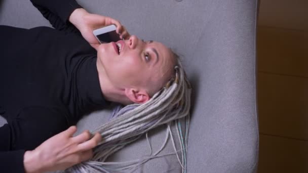 Gros plan pousse de jeune jolie femme caucasienne avec dreadlocks blondes appelant au téléphone couché sur le canapé sur le dos souriant joyeusement et jouant avec ses cheveux — Video