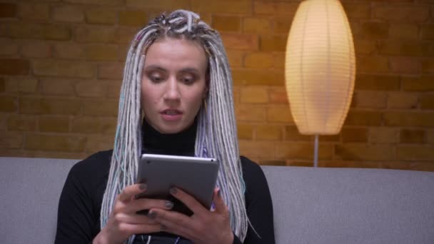 아늑한 아파트에서 소파에 앉아 태블릿을 사용하여 젊은 매력적인 백인 힙스터 여성의 클로즈업 촬영 — 비디오