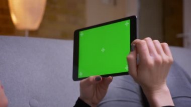 Rahat bir dairede kapalı kanepede yatan yeşil ekran ile tablet tutan kadın ellerin Closeup geri görüş çekimi