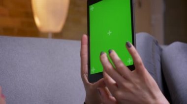 Rahat bir dairede kanepede yatan yeşil ekran ile tablet dikey tutarak kadın ellerin Closeup geri görüş çekimi