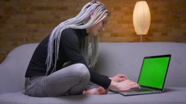 Rahat bir dairede kanepede oturan dizüstü bilgisayar üzerinde çalışan dreadlocks ile genç çekici kafkas hipster iş kadını Closeup ateş