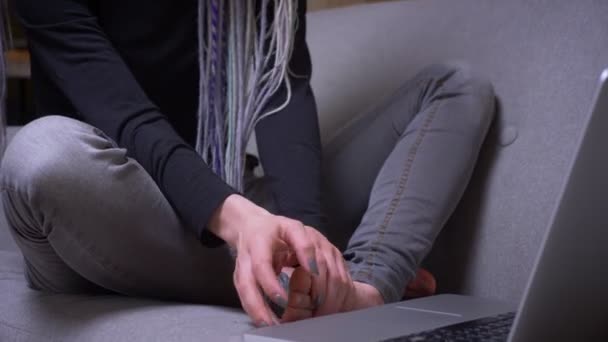 Close-up shoot by camera verplaatsen van de handen typen op de laptop naar jonge aantrekkelijke Kaukasische hipster vrouwelijke gezicht met dreadlocks binnenshuis in een gezellig appartement — Stockvideo