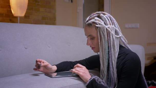 Close-up shoot van jonge aantrekkelijke Kaukasische hipster vrouw met dreadlocks online winkelen op de Tablet met creditcard binnenshuis in een gezellig appartement — Stockvideo