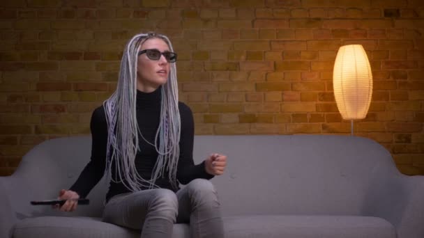Close-up tiro de jovem atraente caucasiano hipster fêmea assistindo a um filme de ação 3D na TV e recebendo um jumpscare sentado no sofá dentro de casa em um aconchegante apartamento — Vídeo de Stock