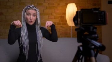 Dreadlocks kamera da konuşurken canlı akışı ve kapalı kanepede oturan gesturing ile genç çekici kadın blogger Closeup ateş
