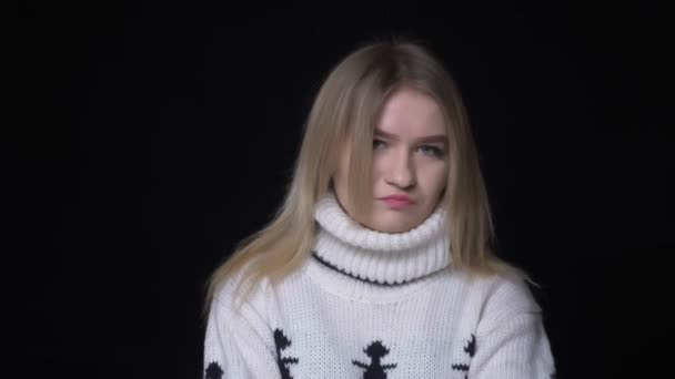 Nahaufnahme einer jungen hübschen kaukasischen Frau im Pullover, die mit dem Kopf wedelt und nicht in die Kamera schaut, deren Hintergrund isoliert auf schwarz ist — Stockvideo