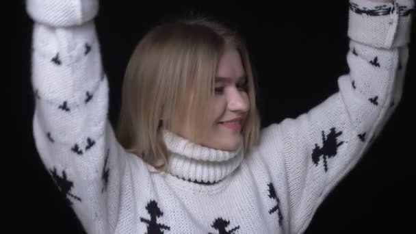 Primer plano de la joven hembra bastante caucásica en suéter bailando felizmente delante de la cámara con fondo aislado en negro — Vídeo de stock