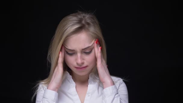 Hübsche junge blonde Geschäftsfrau im weißen Hemd massiert vor schwarzem Hintergrund Kopfschmerzen. — Stockvideo