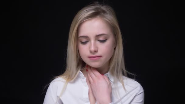 Bonita joven mujer de negocios rubia con camisa blanca toca su cuello sufriendo de dolor de garganta sobre fondo negro . — Vídeos de Stock