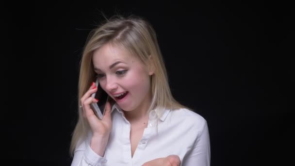 Mulher de negócios bonita e jovem em camisa branca falando no smartphone ri alegremente no fundo preto . — Vídeo de Stock