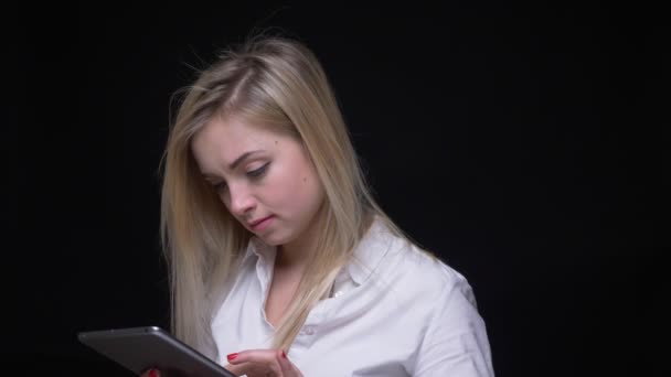 Young blonde businesswoman working with tablet gets confused raises her glance to camera on black background. — 비디오