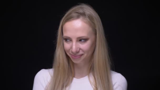 Närbild porträtt av unga vackra blonda kvinnliga leende med förlägenhet tittar på kamera med bakgrund isolerad på svart — Stockvideo