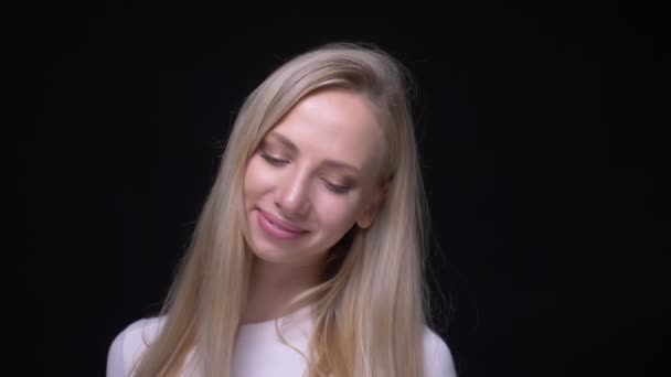 Крупный план портрета молодой красивой блондинки, улыбающейся соблазнительно, играющей волосами, смотрящей в камеру на фоне, изолированном на черном — стоковое видео