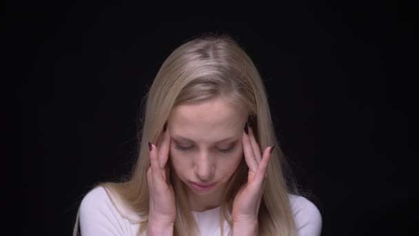 Крупный план портрет молодой симпатичной блондинки, страдающей головной болью и уставшей от фона, изолированного от черного — стоковое видео