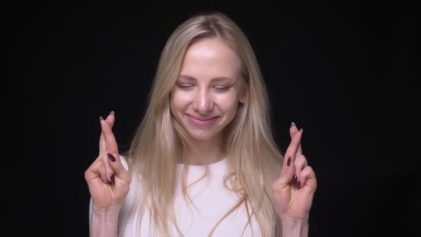 Closeup portré fiatal csinos szőke nő, miután az ujjai keresztbe izgatottan nézi kamera háttérrel izolált fekete — Stock videók