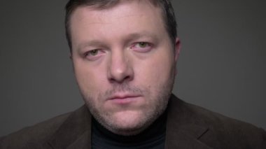 Takım elbiseli esmer orta yaşlı işadamının yakın çekim portresi, gri arka plandaki kameraya barışçıl bir bakış la bakıyor.