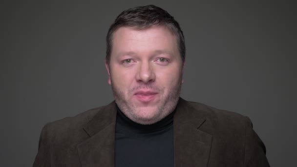 Porträt eines brünetten Geschäftsmannes mittleren Alters im Anzug lächelt positiv belustigt auf grauem Hintergrund. — Stockvideo