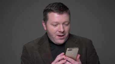 Telefon ile çalışan takım elbiseli esmer orta yaşlı işadamı Portresi son derece şok alır ve gri arka plan üzerinde mutlu.