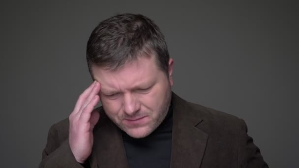 Brunette middle-aged businessman in suit making massage from headache on gray background. — Stock Video