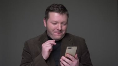 Esmer orta yaşlı işadamı takım elbise akıllı telefon sörf ve duygusal gri arka plan üzerinde tepki.