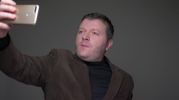 Bruna uomo d'affari di mezza età in giacca e cravatta fare selfie-foto utilizzando smartphone su sfondo grigio . — Video Stock