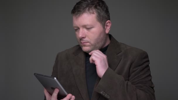 Morena hombre de negocios de mediana edad en traje de trabajo con éxito tableta muestra la pantalla verde de la misma sobre fondo gris . — Vídeo de stock