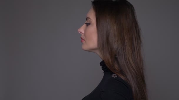 Närbild sida Visa porträtt av vuxna attraktiva kaukasiska kvinnlig svarvning och tittar på kamera med bakgrund isolerad på grå — Stockvideo