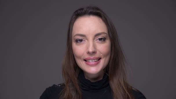 Close-up portret van volwassen aantrekkelijke Kaukasische vrouwelijke gezicht kijken naar camera met vrolijke gezichtsuitdrukking met achtergrond geïsoleerd op grijs — Stockvideo