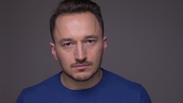 Close-up shoot van jonge knappe Kaukasische mannelijke gezicht kijken naar camera met achtergrond geïsoleerd op grijs — Stockvideo