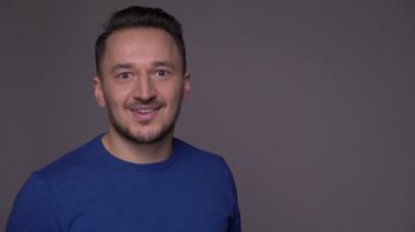Kameraya dönen ve gri izole arka plan ile heyecanla gülümseyen genç yakışıklı kafkas adam Closeup çekim