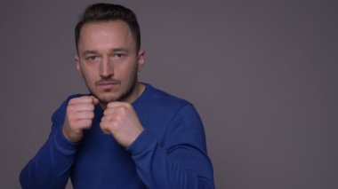 Genç yakışıklı beyaz adam bir kutu savaşçı elleri gri izole arka plan ile kameraya bakarak tekme olmak closeup ateş