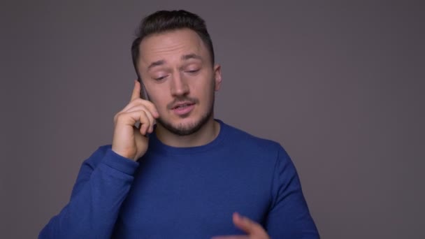 Zbliżenie strzelać młodego przystojnego kaukaski mężczyzna o rozmowę telefoniczną przed kamerą z tła izolowane na szarym — Wideo stockowe