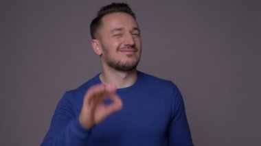 Genç yakışıklı beyaz adam okay işareti gösteren ve gri izole arka plan ile kameraya bakarak gülümseyen Closeup ateş