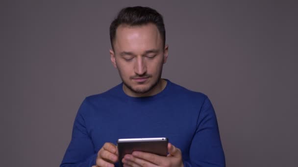 Close-up shoot van jonge knappe blanke man texting op de Tablet en kijken naar camera met achtergrond geïsoleerd op grijs — Stockvideo