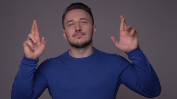 Close-up shoot van jonge knappe blanke man met zijn vingers gekruist worden hoopvol en angstig met achtergrond geïsoleerd op grijs — Stockvideo
