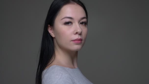 Nahaufnahme einer jungen hübschen kaukasischen Frau, die sich dreht und geradeaus in die Kamera schaut, mit isoliertem Hintergrund auf grau — Stockvideo