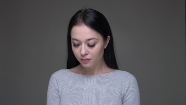 Съемки крупным планом молодой довольно белой женщины, застенчиво смотрящей прямо в камеру на фоне, изолированном на сером — стоковое видео