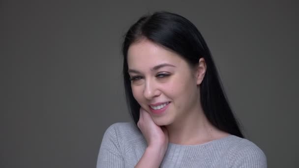 Closeup shoot of young sexy brunette caucasian female seductively smiling flirting while looking straight at camera with background isolated on gray — Stock Video