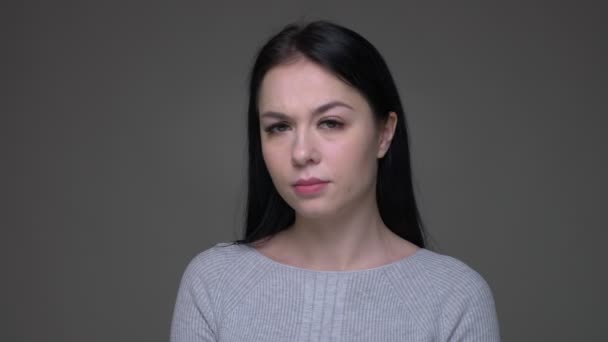 Съемки крупным планом юной брюнетки кавказской женщины, размахивающей головой и не смотрящей прямо в камеру с изолированным на сером фоне — стоковое видео