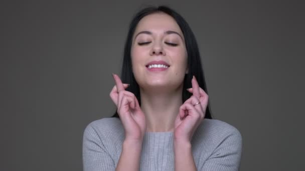 Closeup shoot of young pretty brunette caucasian female having her fingers crossed and being worried with background isolated on gray — Stock Video