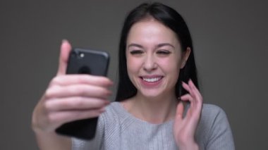 Genç güzel esmer kafkas kadın gri izole arka plan ile merhaba sallayarak telefonda bir görüntülü arama olan Closeup ateş