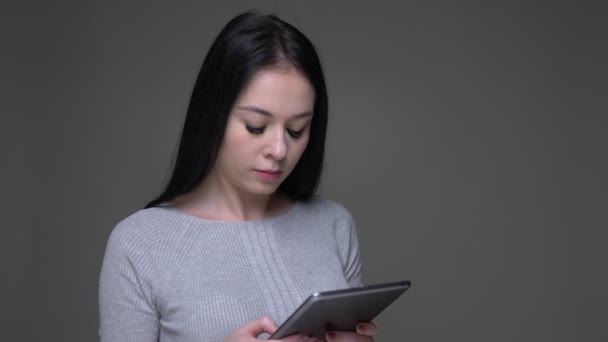 Primer plano de brote de joven guapa morena caucásica hembra utilizando la tableta con fondo aislado en gris — Vídeo de stock