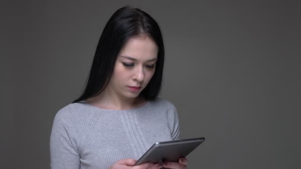 Närbild shoot av unga ganska Brunette kaukasiska kvinna surfar på tabletten med bakgrund isolerade på grått — Stockvideo