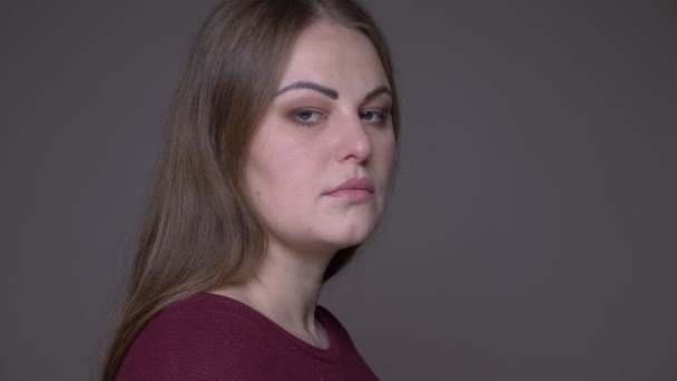 Closeup side view portarit of young overweight caucasian female looking at camera with background isolated on gray — Stock Video