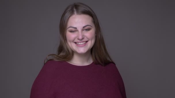Close-up portarit van jonge overgewicht blanke vrouwelijke glimlachend vrolijk kijken naar camera met achtergrond geïsoleerd op grijs — Stockvideo
