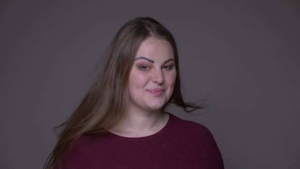 Closeup portarit of young overweight caucasian female turning to camera with her hair fluttering and laughing happily with background isolated on gray — Stock Video