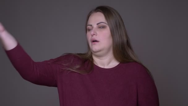 Closeup portarit s mladou nadváhou bělošskou ženskou, která se nemaskuje a zlobí na kameru s pozadím izolovaným na šedé — Stock video