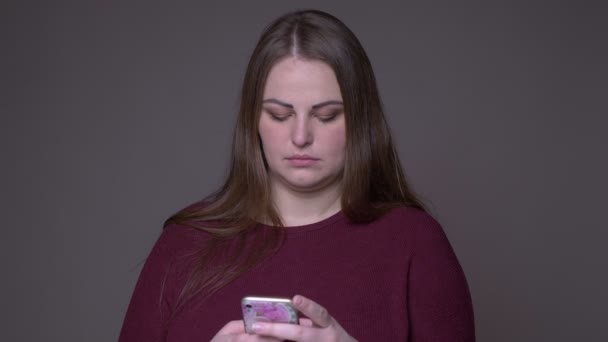 Close-up portarit van jonge overgewicht blanke vrouw met behulp van de telefoon met achtergrond geïsoleerd op grijs — Stockvideo