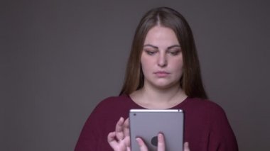 Tableti kullanarak ve gri üzerinde izole arka plan ile kameraya yeşil ekran gösteren genç kilolu beyaz kadın Closeup portarit